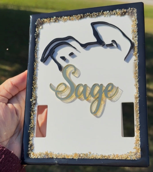 Decorative light switch cover with 'Sage' and a dog silhouette, held outdoors.