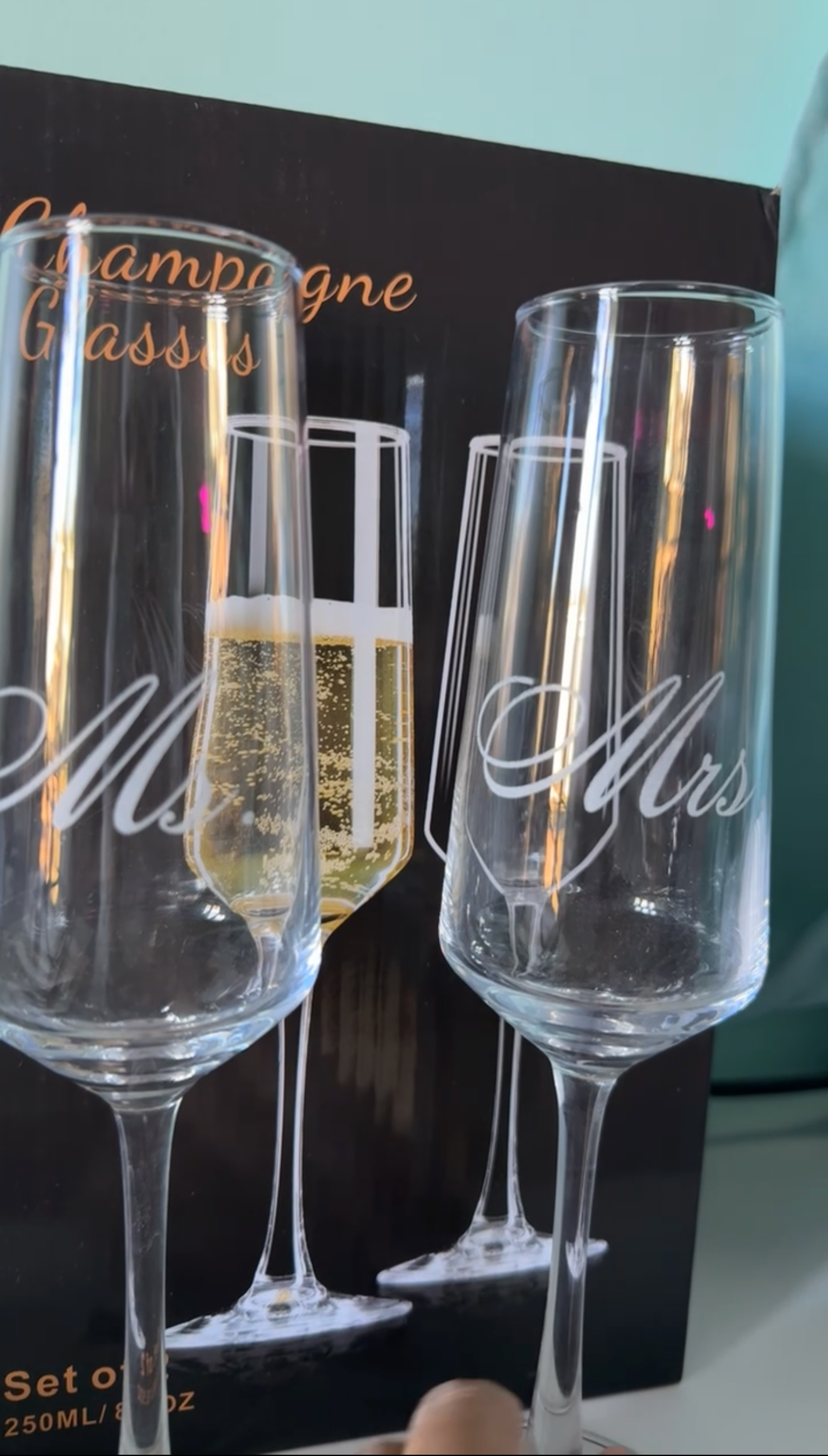 Two champagne flutes labeled 'Ms.' and 'Mrs.' with a box in the background.